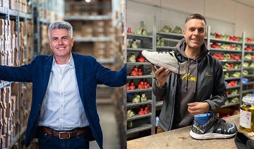 Links ein Mann in einem Anzug in einem Lager mit Kartons, rechts ein Mann in dunkler Kleidung mit einem Schuh in der Hand, im Hintergrund Regale mit Schuhen.
