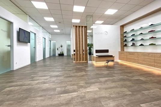 Innenansicht eines modernen Showrooms mit Holzfußboden, einer Sitzgelegenheit und einer beleuchteten Schuhpräsentation an der Wand.